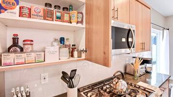 Una cocina con estufa a gas, microondas y varios utensilios de cocina en estantes.