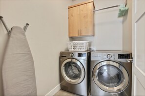 A laundry area with two stacked front-loading washing machines, a wooden cabinet above, and a hanging laundry rack.