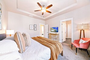 Un dormitorio con cama, ventilador de techo, televisor, lámpara y una silla.