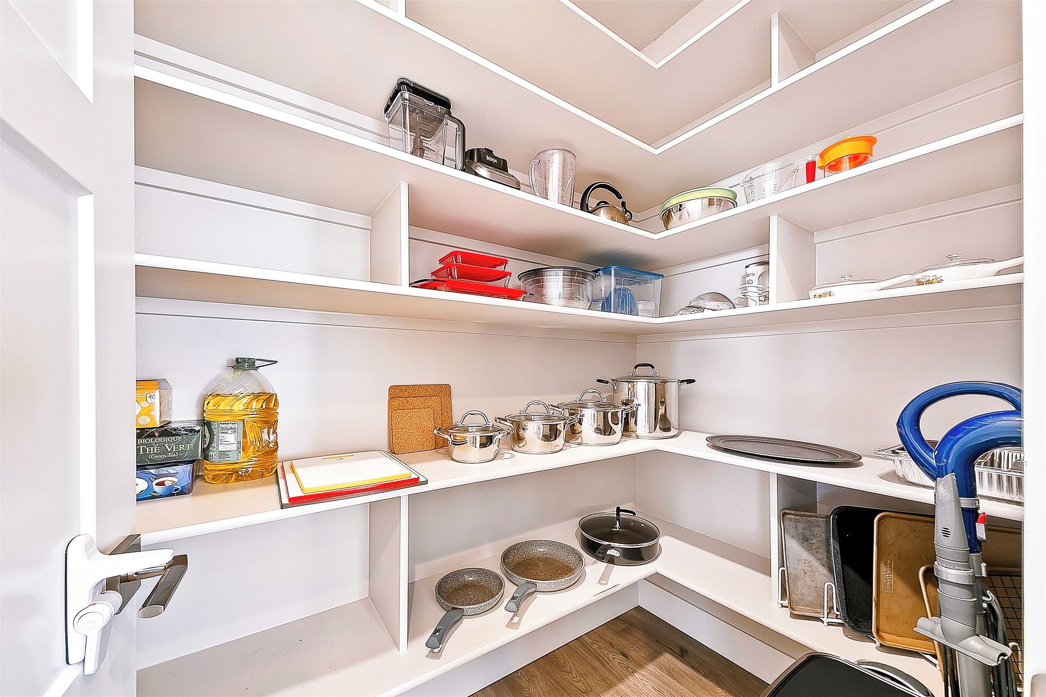 Una cocina con estantes blancos, distintos utensilios de cocina y una aspiradora azul.
