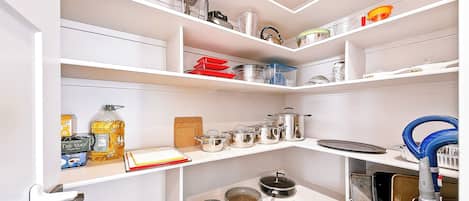 Una cocina con estantes blancos, distintos utensilios de cocina y una aspiradora azul.