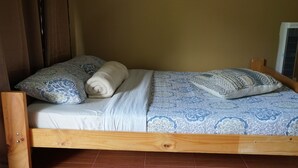 A wooden bed with patterned bedding and pillows, a wooden headboard, and a tiled floor.