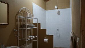 A bathroom with a white tiled shower, a metal towel rack with towels, a toilet, and a mirror.