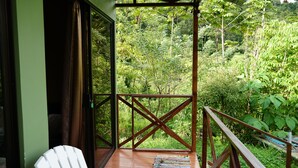 A balcony with a wooden railing, a white chair, and a view of dense greenery.