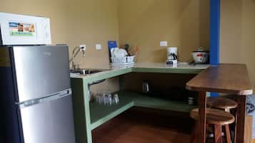 Una cocina compacta con refrigerador, lavamanos y una mesa de madera.