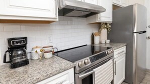 Eine moderne Küche mit weißen Schränken, einem Edelstahlkühlschrank, einer schwarzen Kaffeemaschine und einer Arbeitsplatte aus Granit.