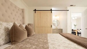 Ein Schlafzimmer mit einem großen Bett, einem Holzschrank, einem runden Spiegel und einer Essecke im Hintergrund.