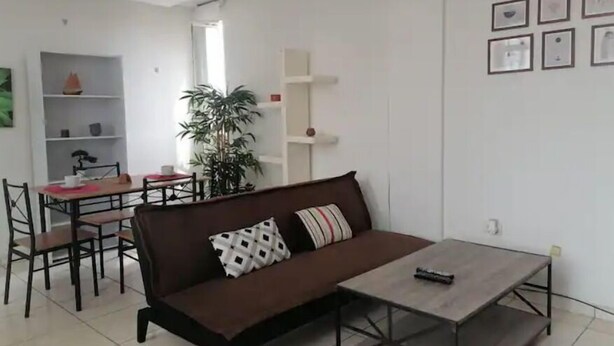 A modern living room with a brown sofa, a coffee table, and a dining area with a red table and chairs.