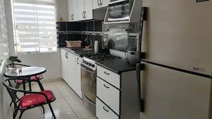A modern kitchen with white cabinets, a microwave, a Samsung refrigerator, a gas stove, and a small dining table with red chairs.