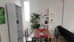 A dining area with a table, chairs, a potted plant, and a bookshelf.