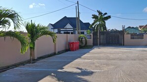 A gated residential area with a paved driveway, palm trees, and houses with varied roofing styles. - Entire two bedroom apartment in  Dar es salaam (Dar es Salaam(city))