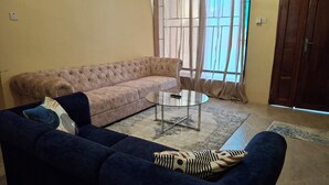 A living room with a beige sofa, a dark blue sofa, and a glass coffee table. - Entire two bedroom apartment in  Dar es salaam (Dar es Salaam(city))