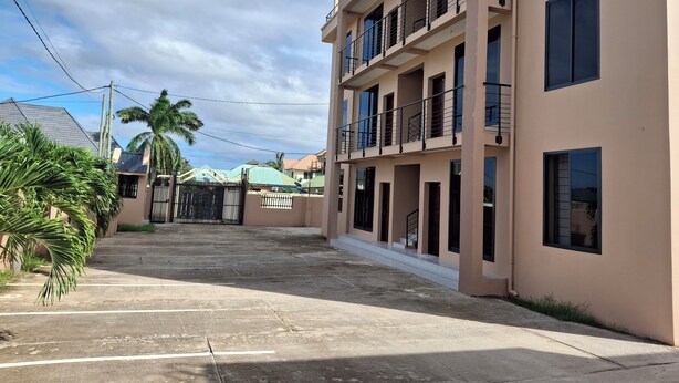 A multi-story building with balconies, a gated entrance, and a paved driveway. - Entire two bedroom apartment in  Dar es salaam (Dar es Salaam(city))