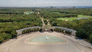 Una amplia plaza abierta con una fuente central, rodeada de abundante vegetación y palmeras.
