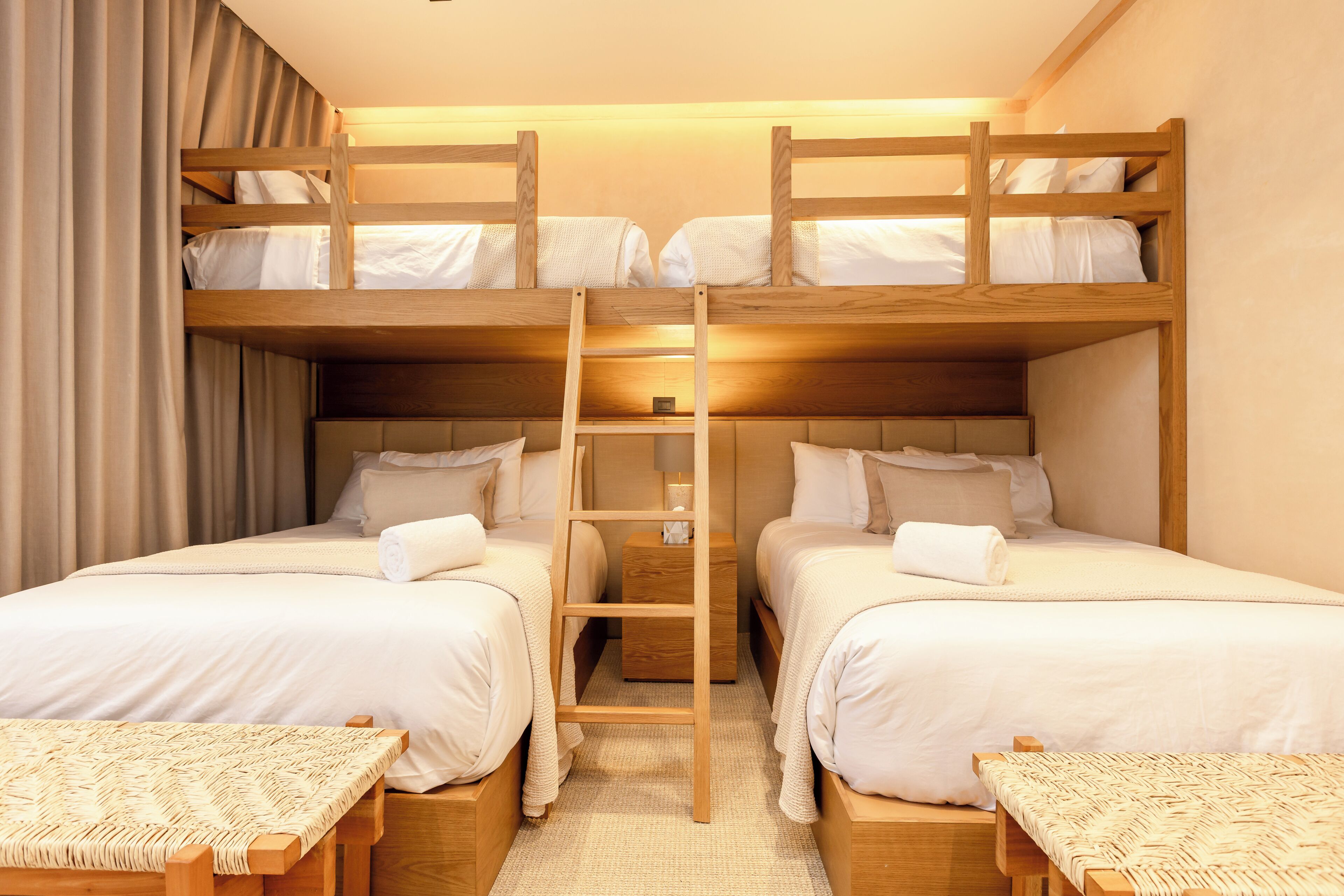 Habitación con literas, una escalera, dos mesitas de noche y un tapete tejido en el suelo.
