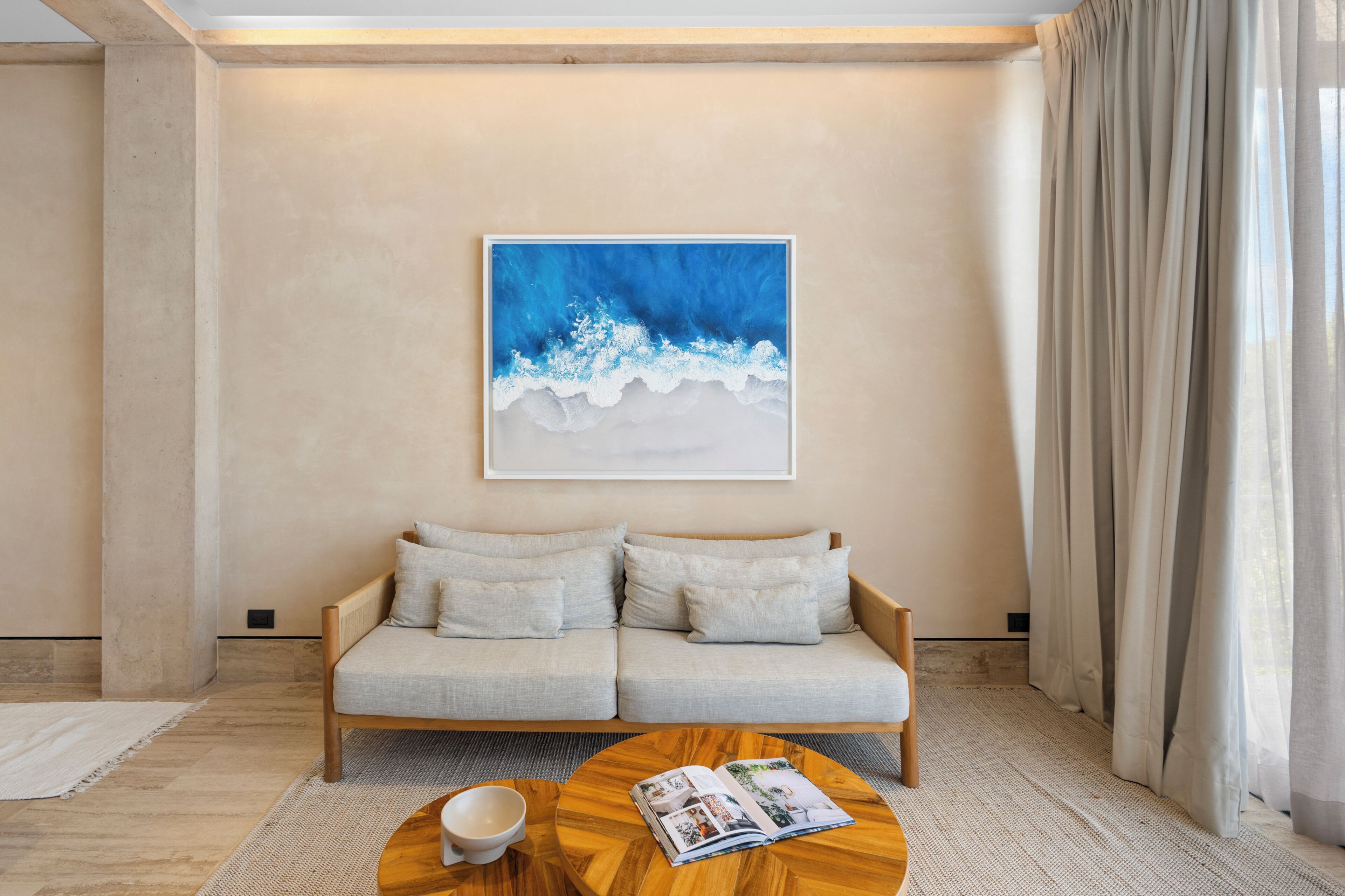Una sala de estar moderna con un sofá color beige, una mesa de centro de madera y una obra de arte enmarcada en la pared.