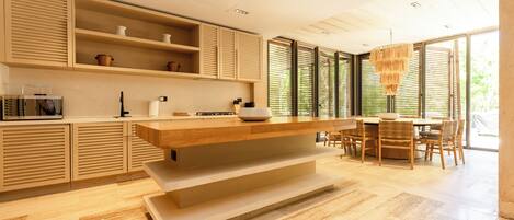 A modern kitchen with wooden cabinetry, a central island, and a dining area with chairs and a table.