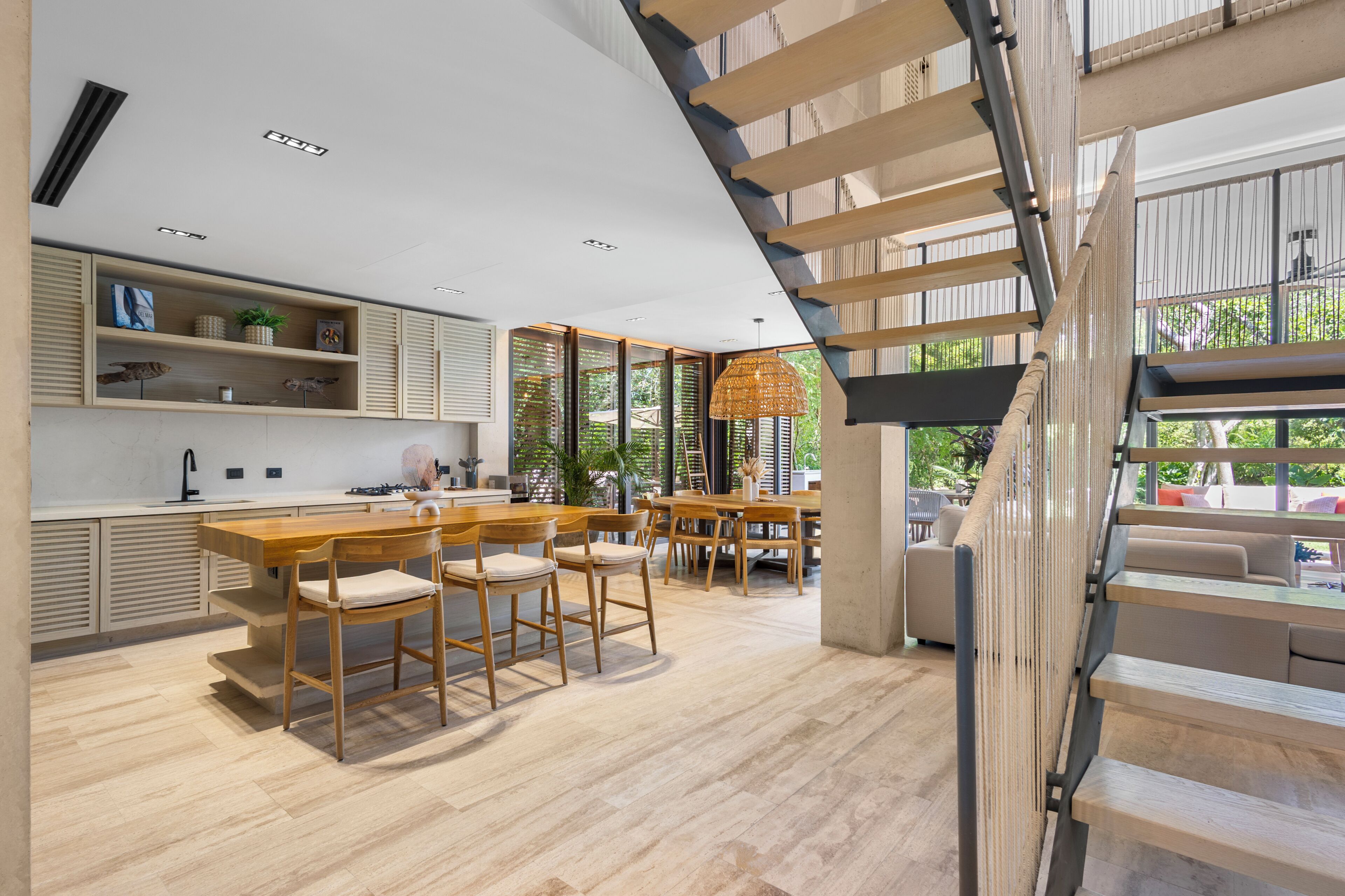 Eine moderne Küche mit Holzschränken, ein Essbereich mit großem Tisch und Stühlen sowie eine Treppe, die in ein Obergeschoss führt.