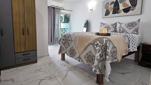 Ein Schlafzimmer mit Bett, Deckenventilator, Kleiderschrank und angrenzendem Badezimmer, durch eine Glastür sichtbar.