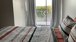 Ein Schlafzimmer mit Bett, einem fenster mit Vorhängen, einer Klimaanlage und einem Balkon mit Geländer.