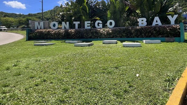 Schild für Montego Bay mit blauem Himmel und üppiger Vegetation im Hintergrund.
