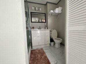 Een badkamer met een wit wastafel, spiegel en toilet. Er ligt een bruin vloerkleed op de vloer.