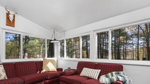 A cozy room with a red plaid sofa, a wooden wall decoration, and large windows offering a view of a forest.