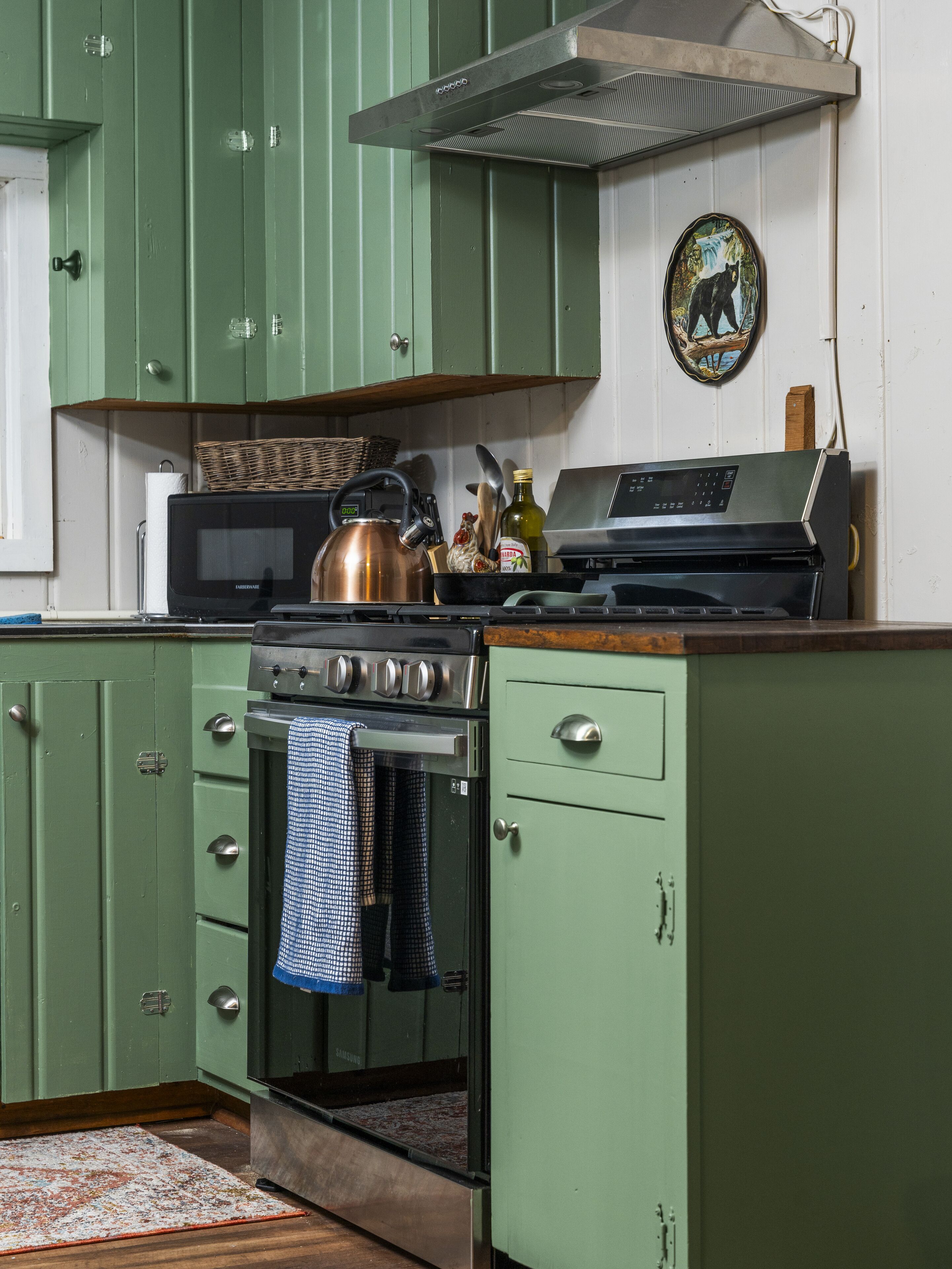 A kitchen with green cabinets, a microwave, a kettle, and a Samsung oven.