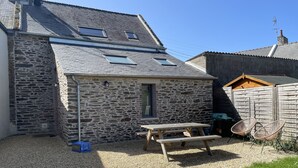 A stone building with a sloped roof, a wooden picnic table, and a fenced area.