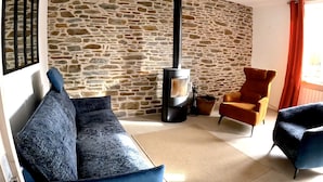 A living room with a stone wall, a black fireplace, a blue sofa, and an orange armchair.