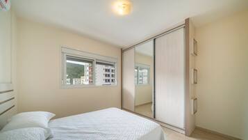 Quarto com cama, janela, porta de correr e vista para prédios.