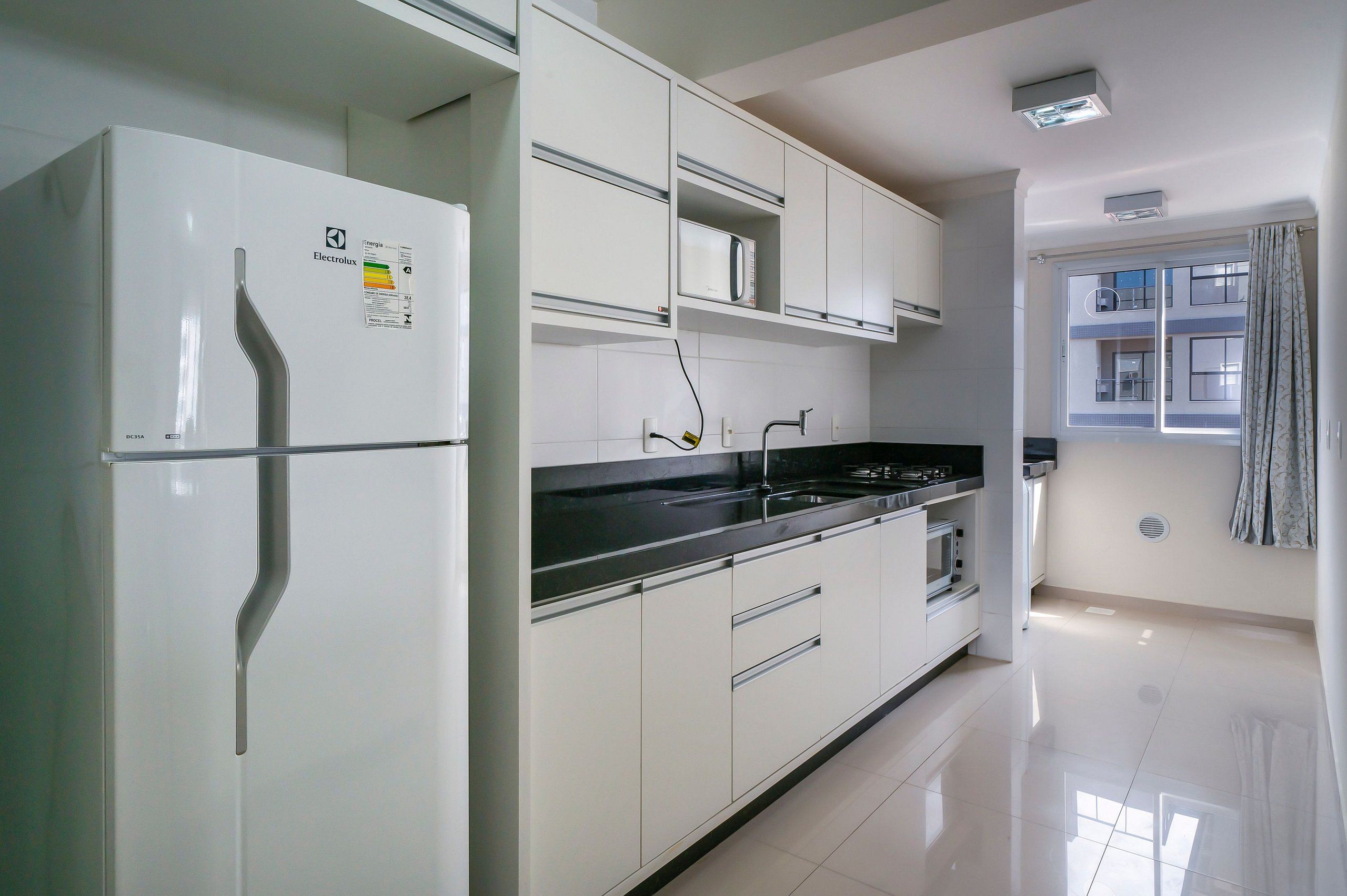A modern kitchen with white cabinetry, a built-in microwave, and a stainless steel sink.