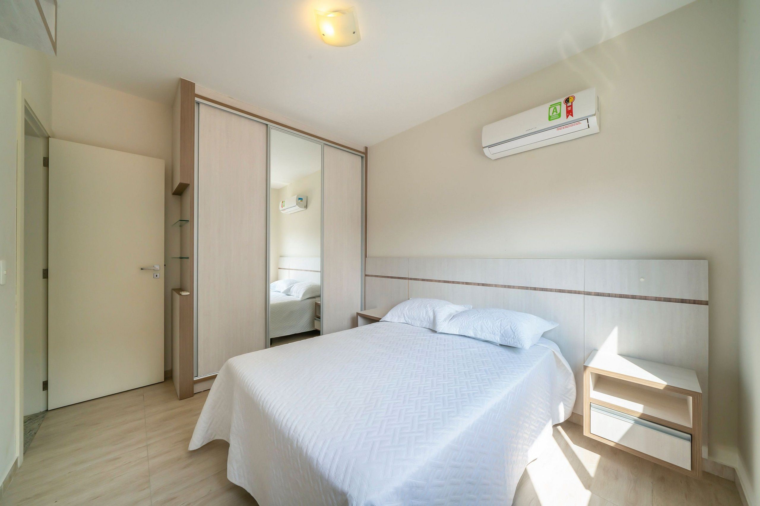Quarto com cama, mesa de cabeceira, guarda-roupa e ar condicionado.