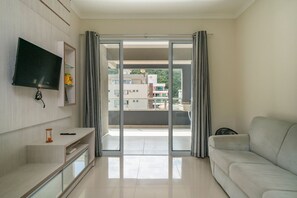 A modern living room with a flat-screen TV, a sofa, and a sliding glass door leading to a balcony.