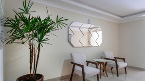 Une pièce moderne avec une plante en pot, deux fauteuils blancs, une petite table ronde et un miroir mural aux motifs géométriques.
