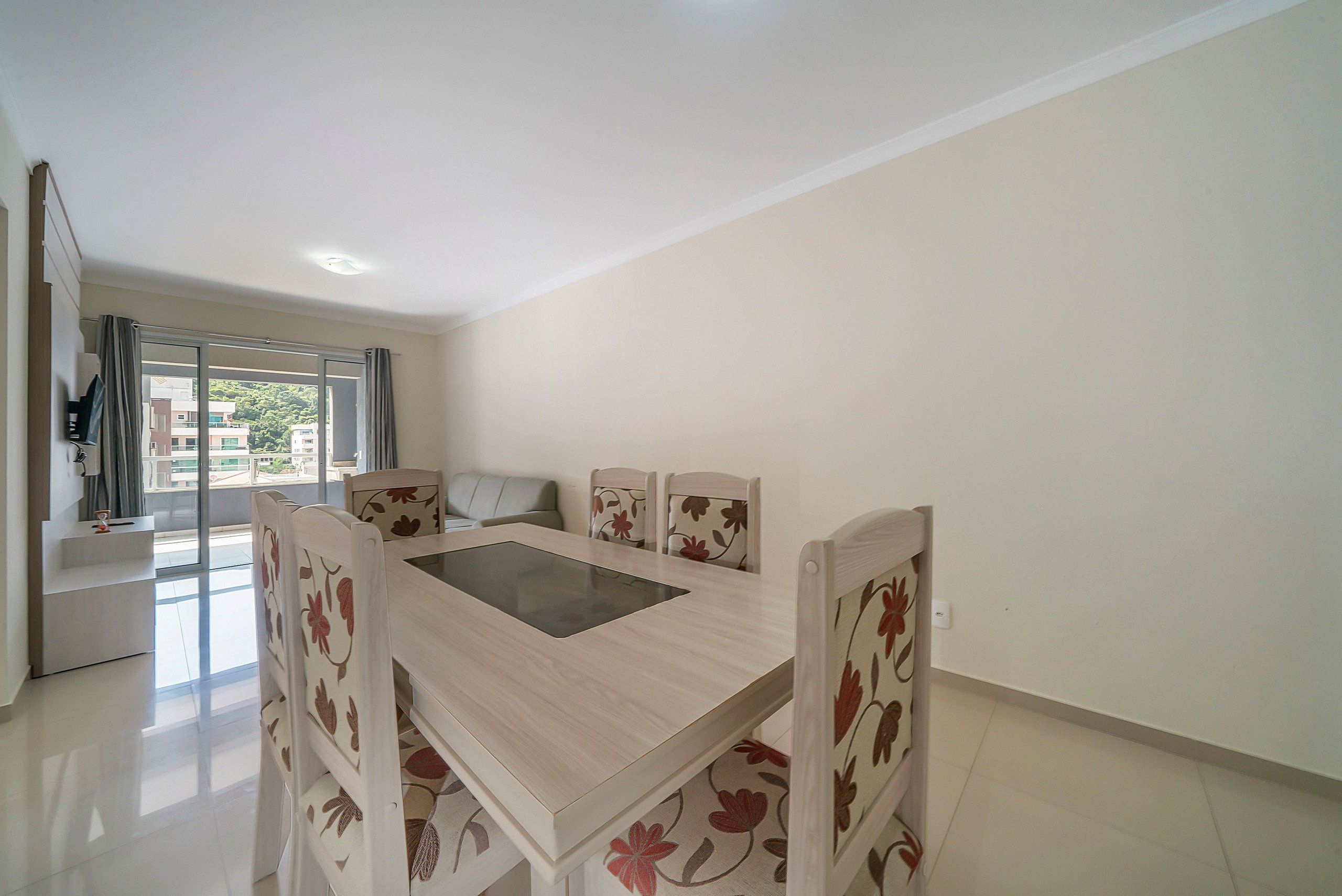 Uma área de refeições moderna com mesa e cadeiras de madeira, vista para o exterior e uma varanda.