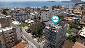 Une vue urbaine mettant en valeur un bâtiment imposant portant l’inscription « BOAVIS », doté d’une terrasse sur le toit et entouré d’autres immeubles résidentiels et commerciaux, avec une vue sur la mer en arrière-plan.