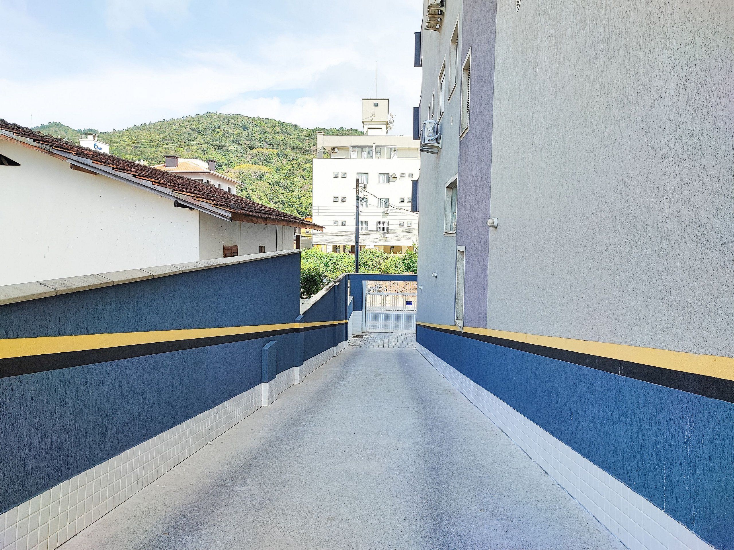 A narrow alleyway with blue and yellow painted walls, leading to a building with a tiled roof.