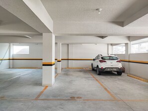 A parking garage with concrete pillars, a white car parked, and yellow and black painted lines on the walls.