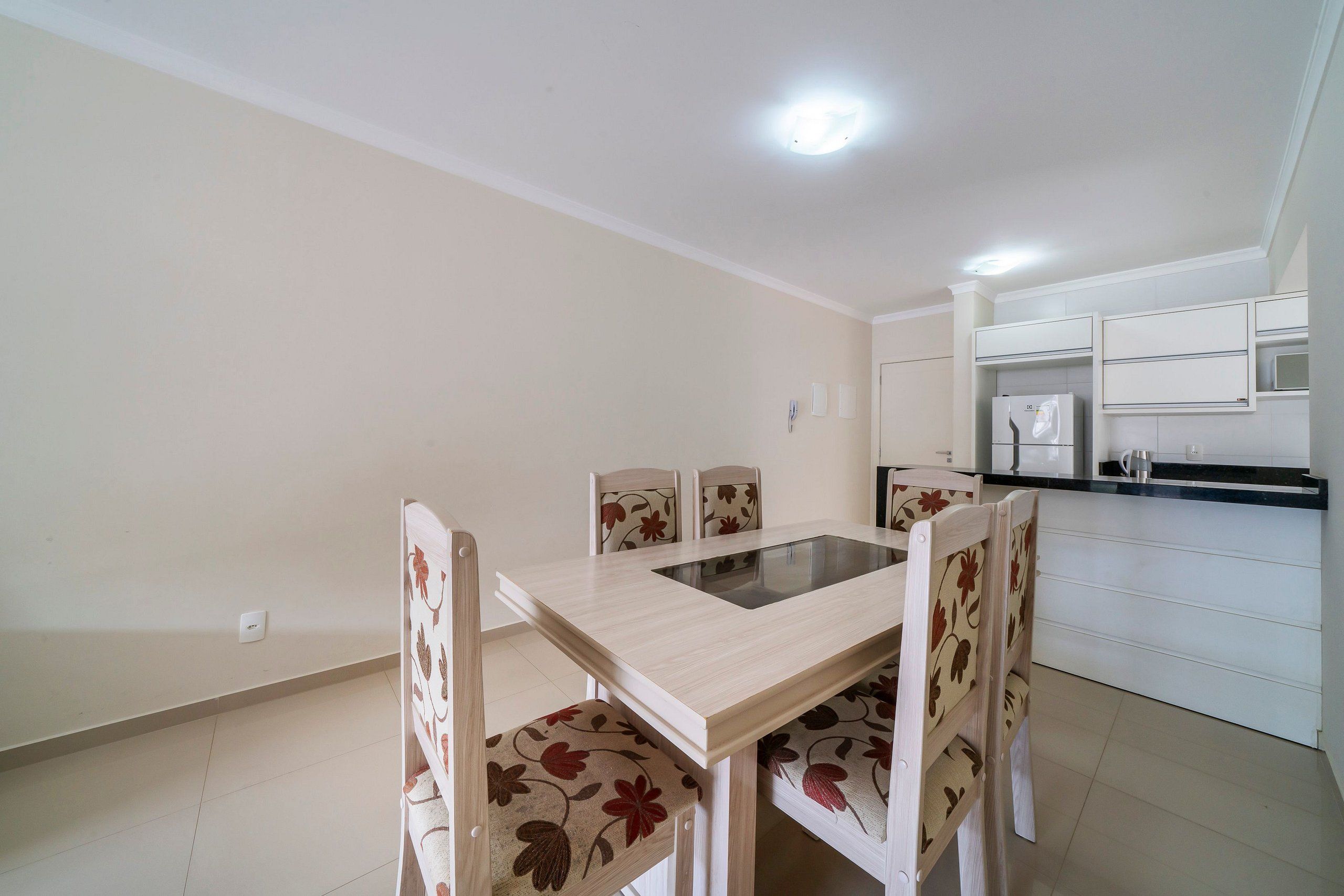 A dining area with a table and chairs, a kitchen with white cabinets, and a ceiling light.