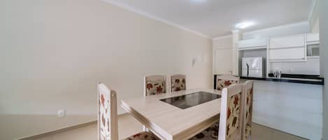 A dining area with a table and chairs, a kitchen with white cabinets, and a ceiling light.