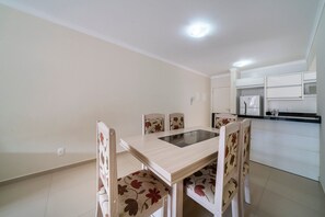 A dining area with a table and chairs, a kitchen with white cabinets, and a ceiling light.