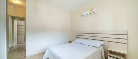A bedroom with a bed, bedside tables, a wall-mounted air conditioner, and a door leading to another room.