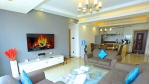 A modern living room with sofas, a glass coffee table, and a flat-screen TV displaying a fireplace.