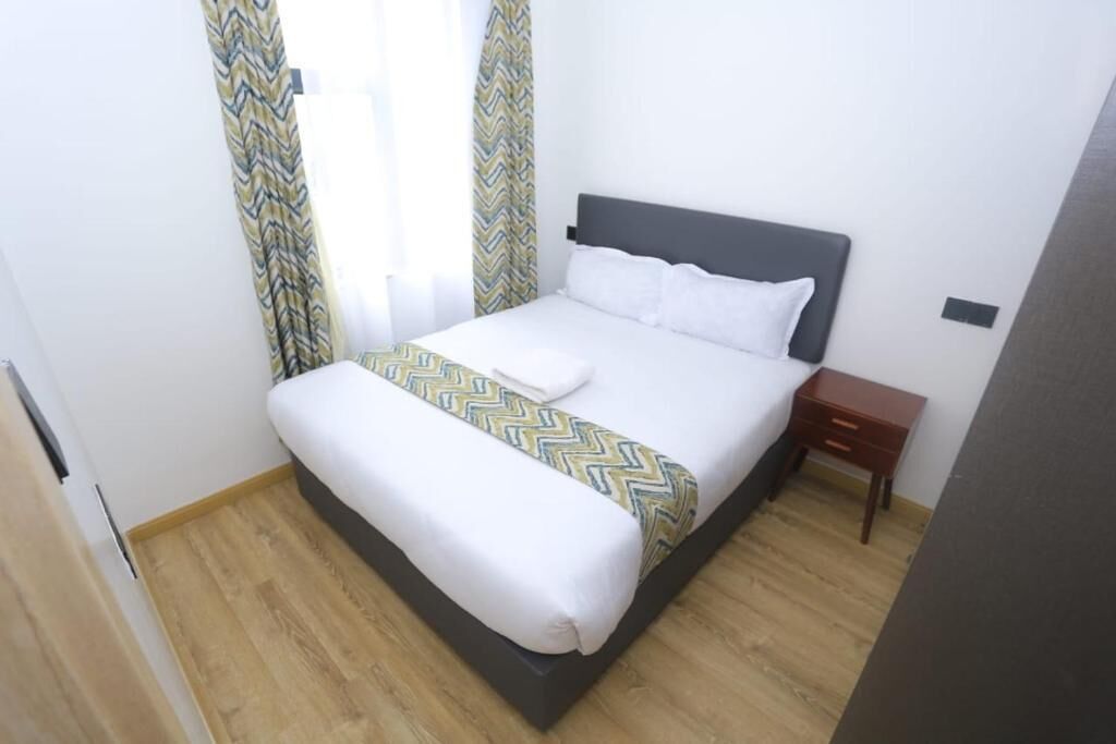 Uma cama bem arrumada com um cobre-leito estampado, uma mesa de cabeceira e cortinas na janela.