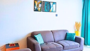 A living room with a brown leather sofa, teal cushions, a small table, and abstract art on the wall.