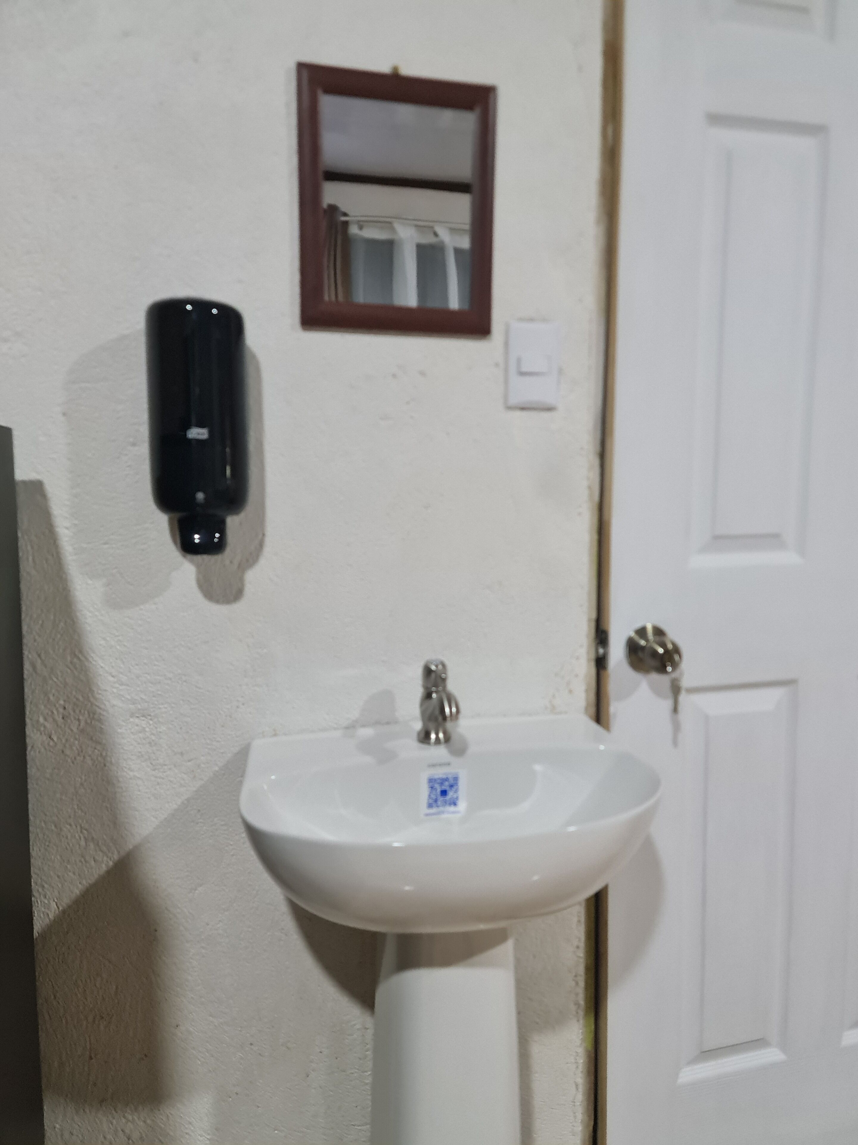 Un lavabo blanco con un grifo, un espejo encima y una puerta a la derecha.