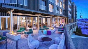A modern hotel with a covered outdoor seating area featuring sofas and chairs, a fire pit, and a view of a snowy landscape. - Ski-in/Ski-out Canyon Haus Modern 1 bedroom- Pool, Hot Tub, Gym (Park City)