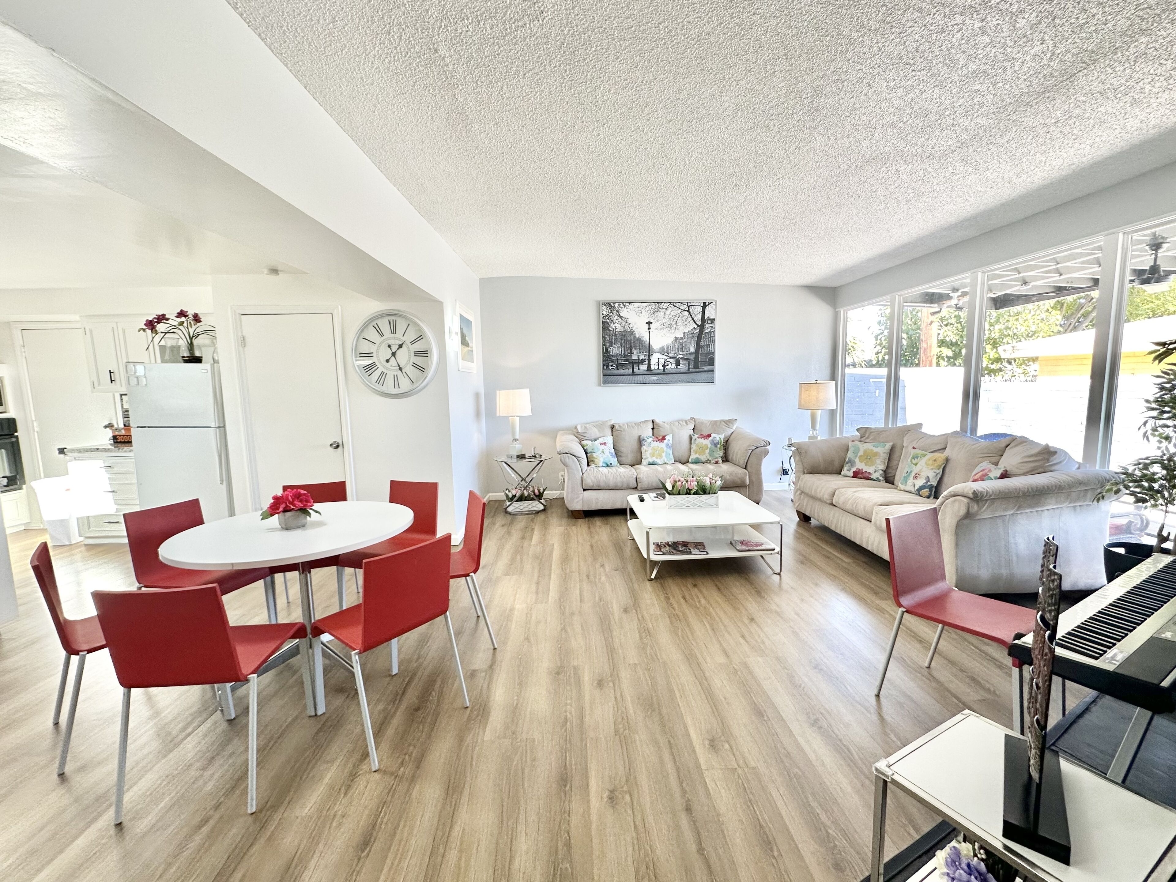 A modern living room with a dining area, a piano, and a large window.