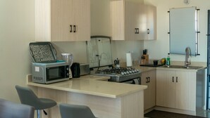 Una cocina moderna con alacenas de madera clara, microondas, tostadora y estufa a gas.